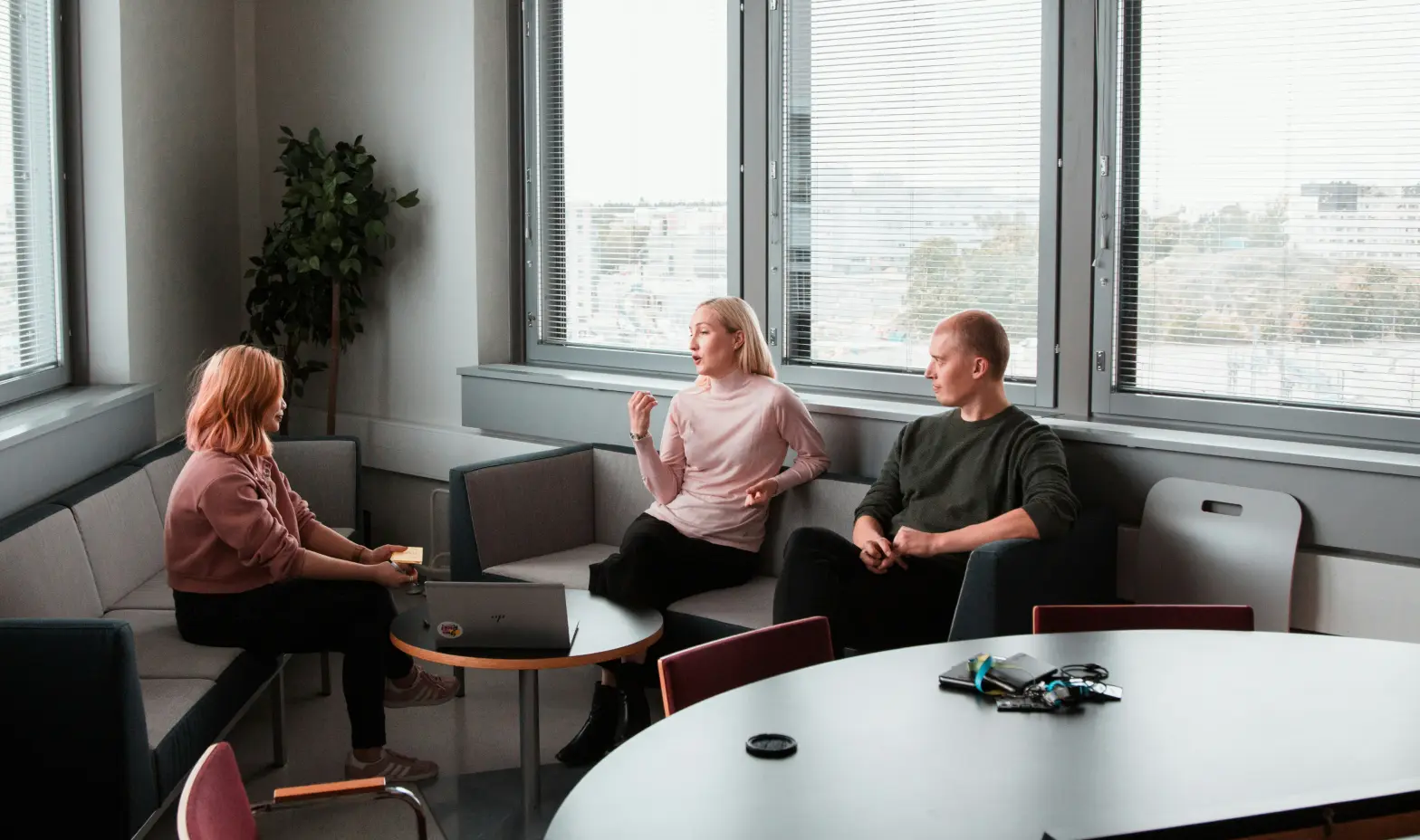 Three people engaged in discussion while sitting around a table in a modern office setting.
