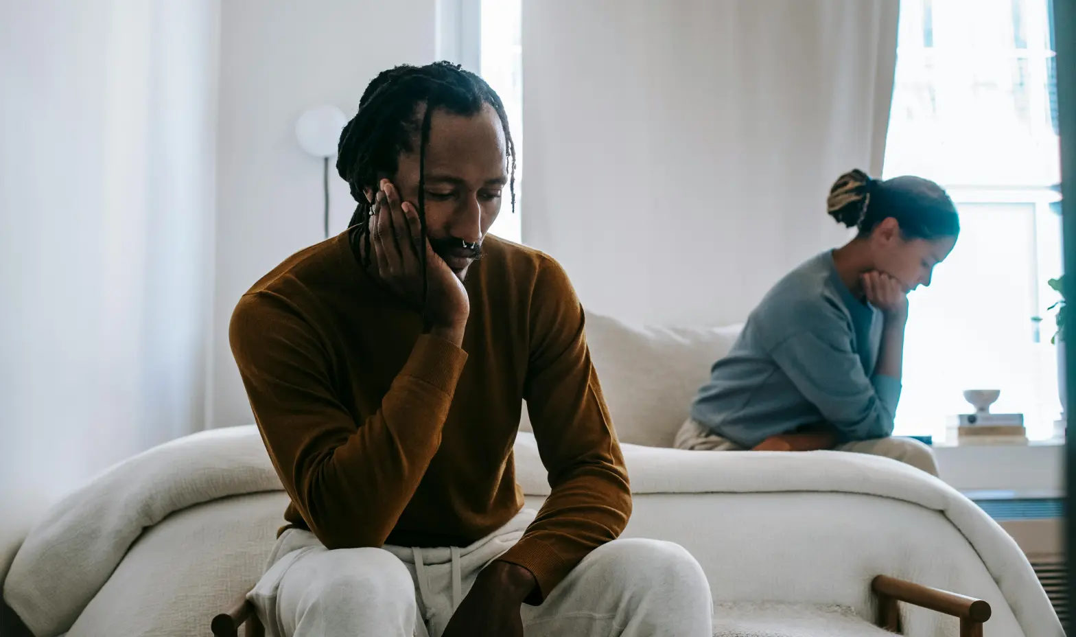 A couple sits on a bed in a warm room, sharing a moment of comfort and connection.