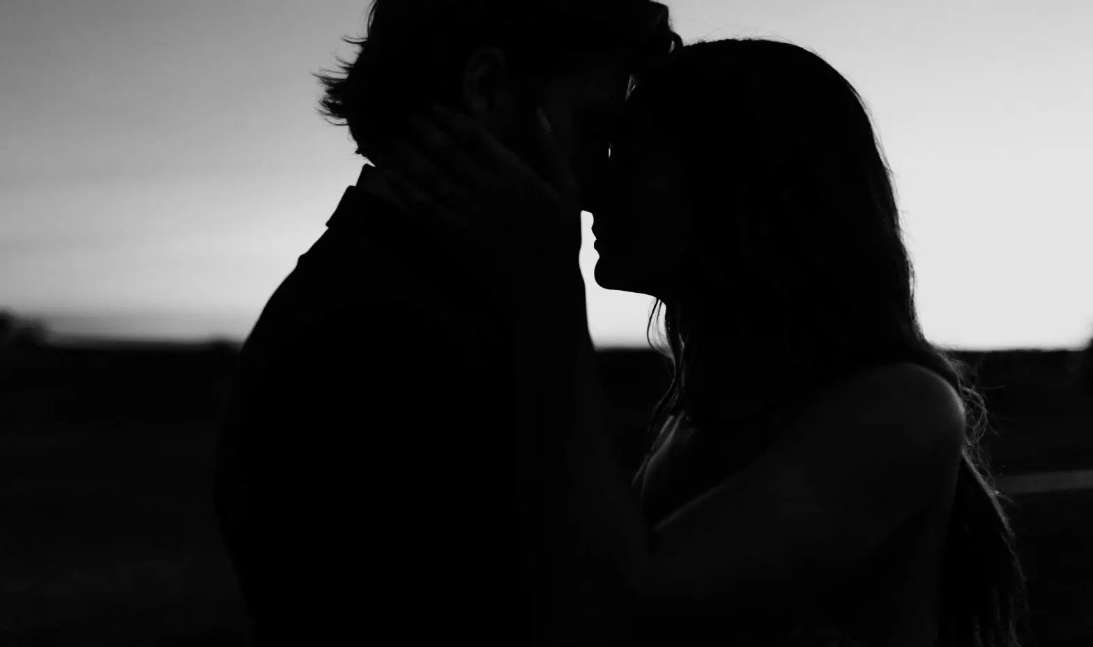 A dark silhouette of a bride and groom kissing, capturing a tender moment of love and celebration.