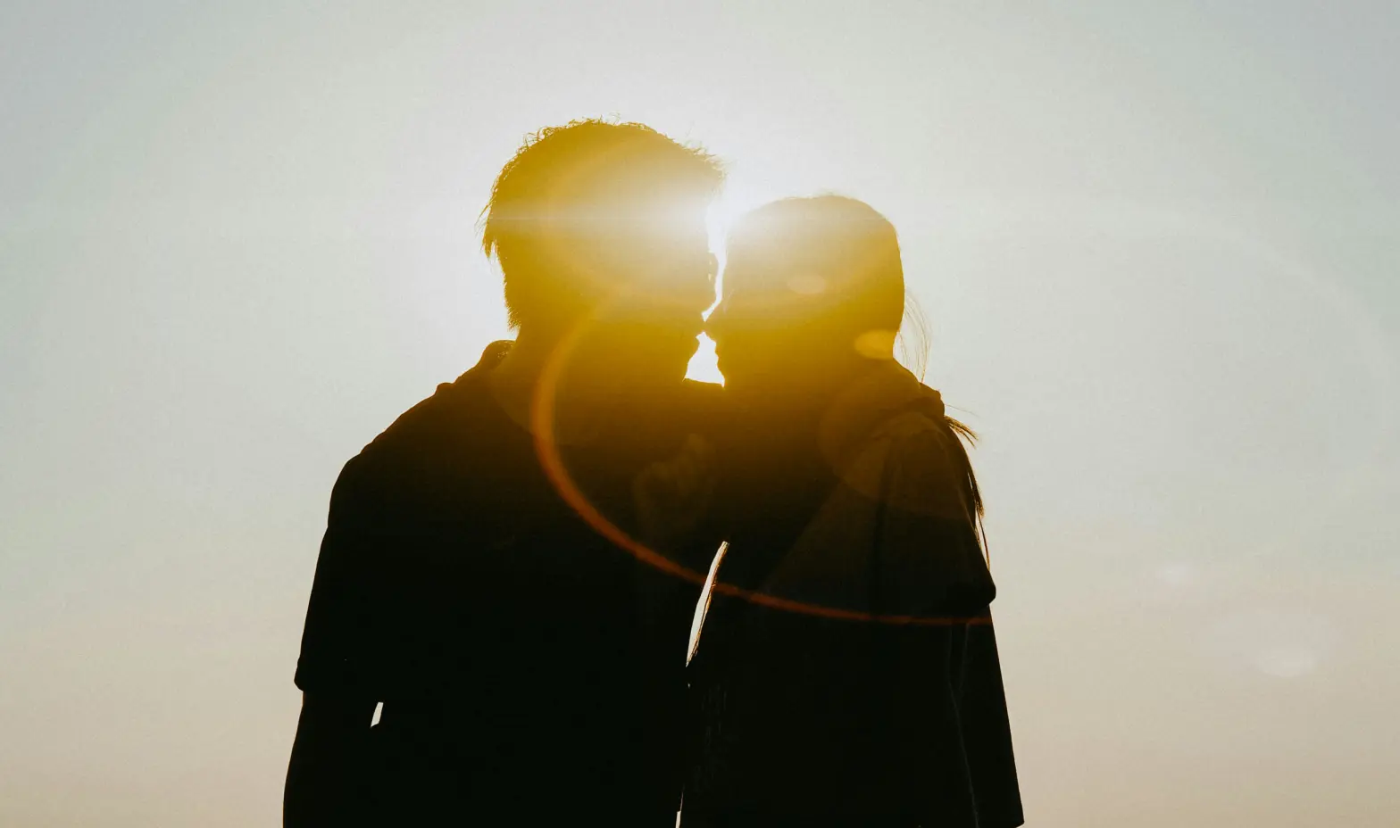 A couple's silhouette kissing as the sun sets behind them, creating a romantic scene.