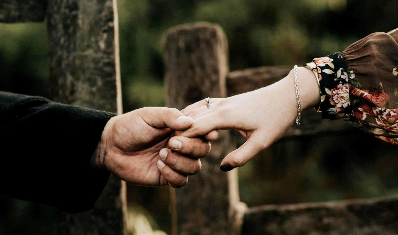 A happy couple clasping hands, posing together in front of a weathered wooden fence.
