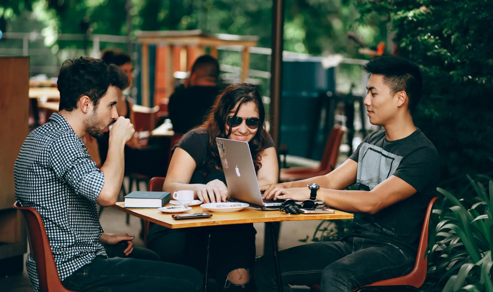 A trio of individuals seated at a table, engaged with their laptops, sharing ideas and working together.