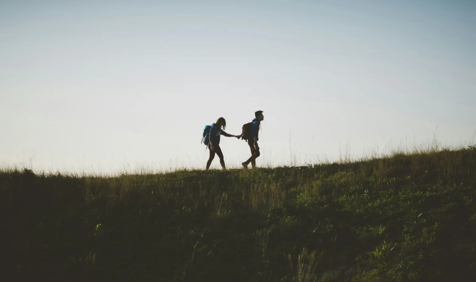 Two people walking hand in hand on a grassy hill, enjoying a sunny day together.