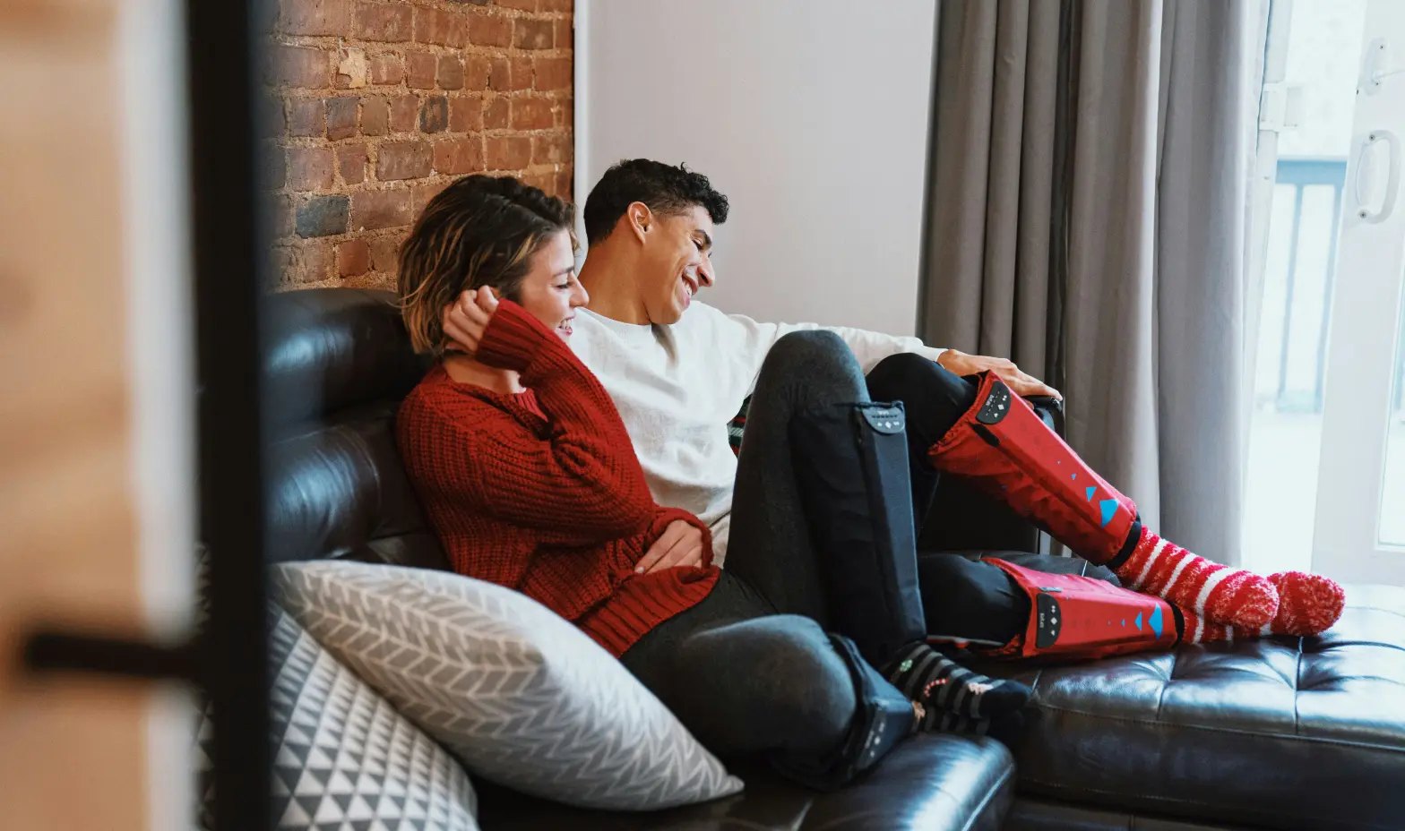 A couple sits comfortably on a couch, chatting, with a textured brick wall behind them.