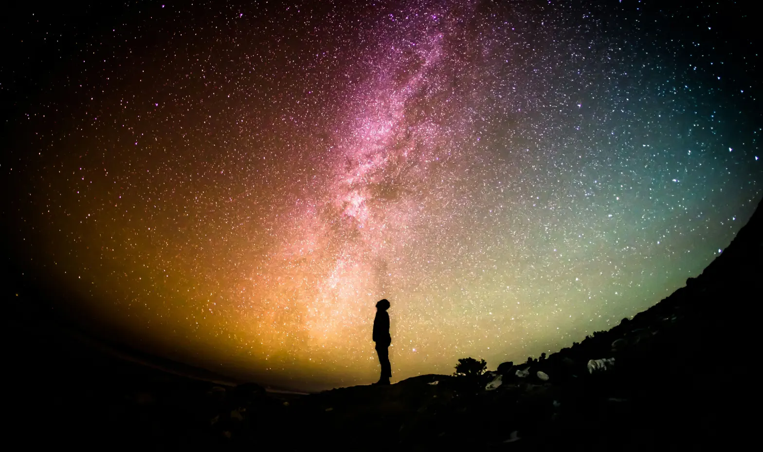 A person stands against a vibrant, colorful sky, showcasing shades of pink, orange, and blue.