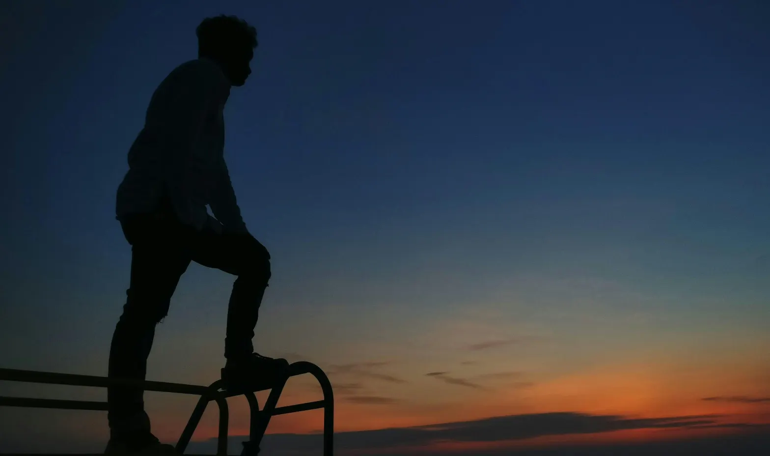 A man standing on a railing at sunset