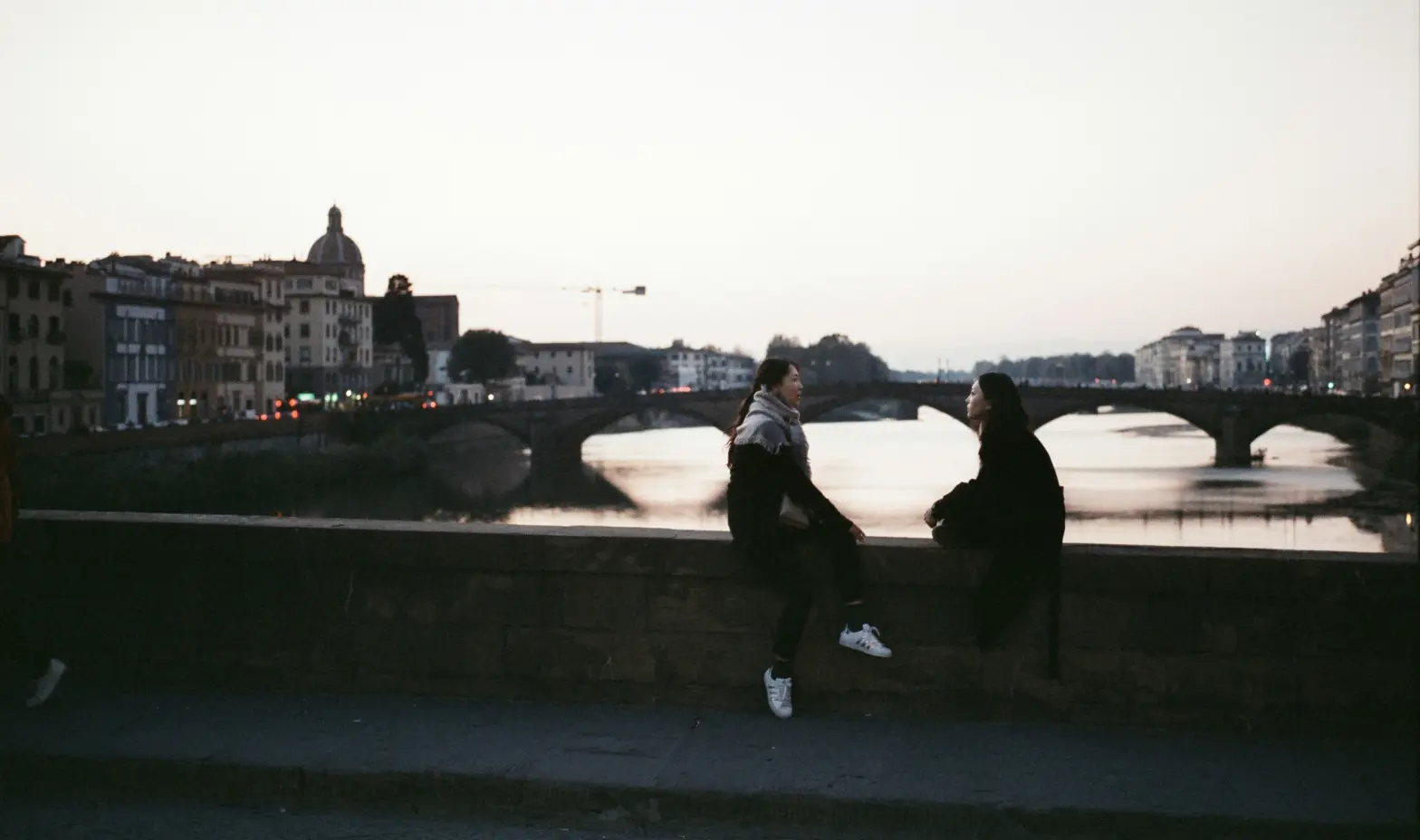 Two people sitting on a wall by a river, enjoying the view and each other's company.