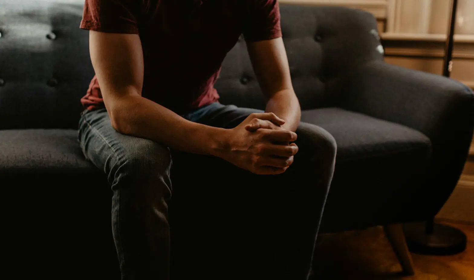 In a dark room, a man relaxes on a couch, surrounded by shadows and soft lighting.
