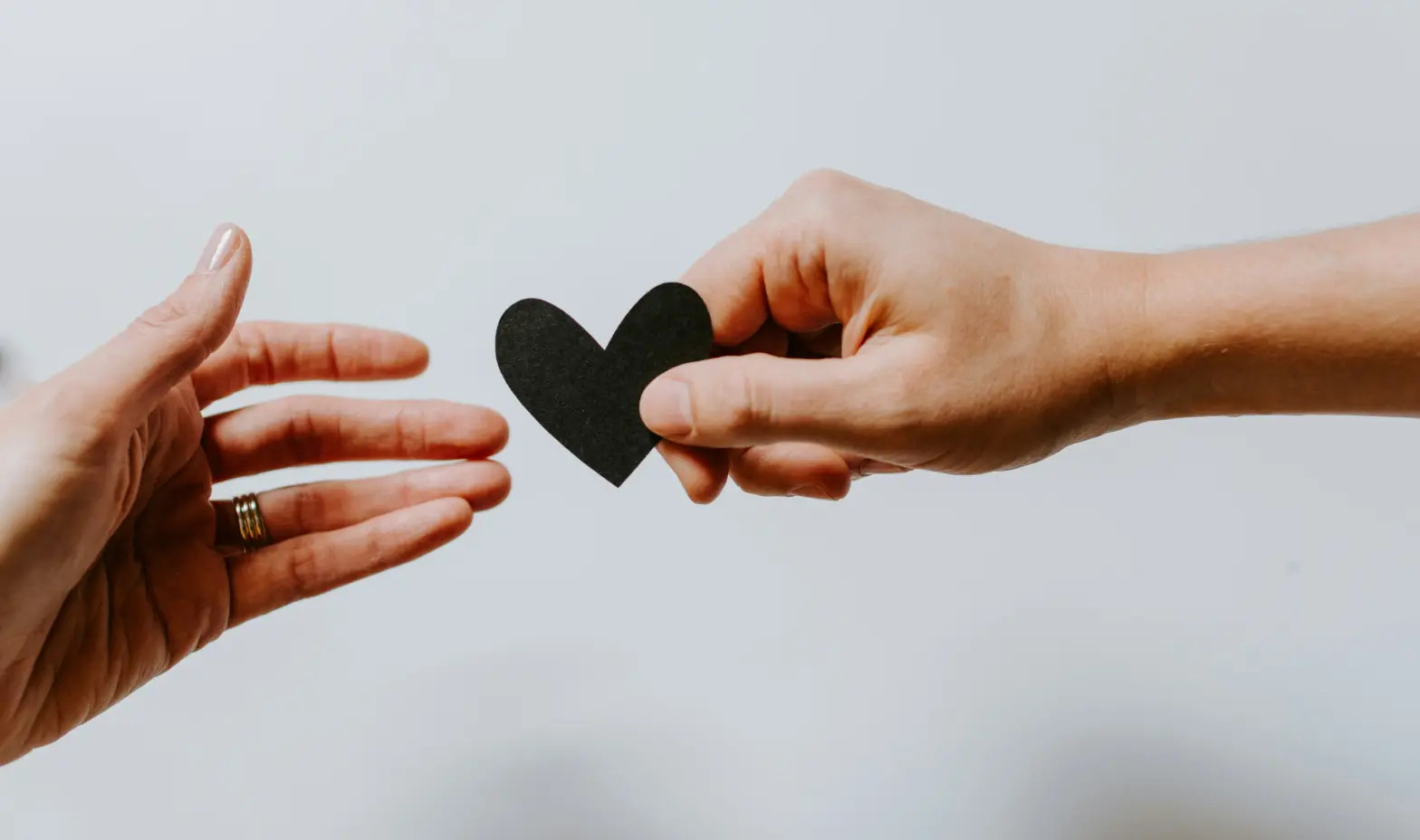 Two hands gently hold a black heart-shaped paper, symbolizing love or affection.