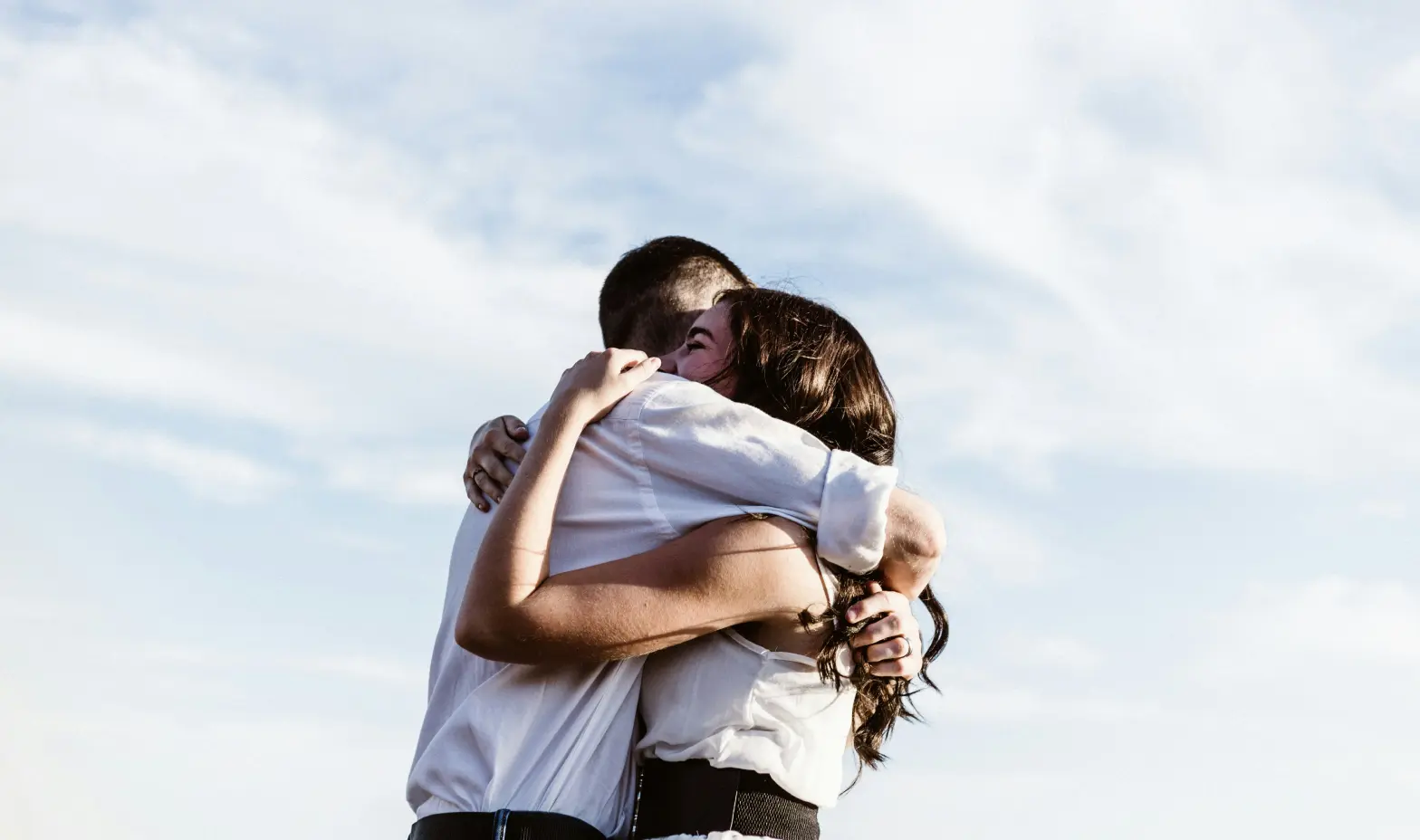 A couple shares a warm embrace against a bright blue sky backdrop.