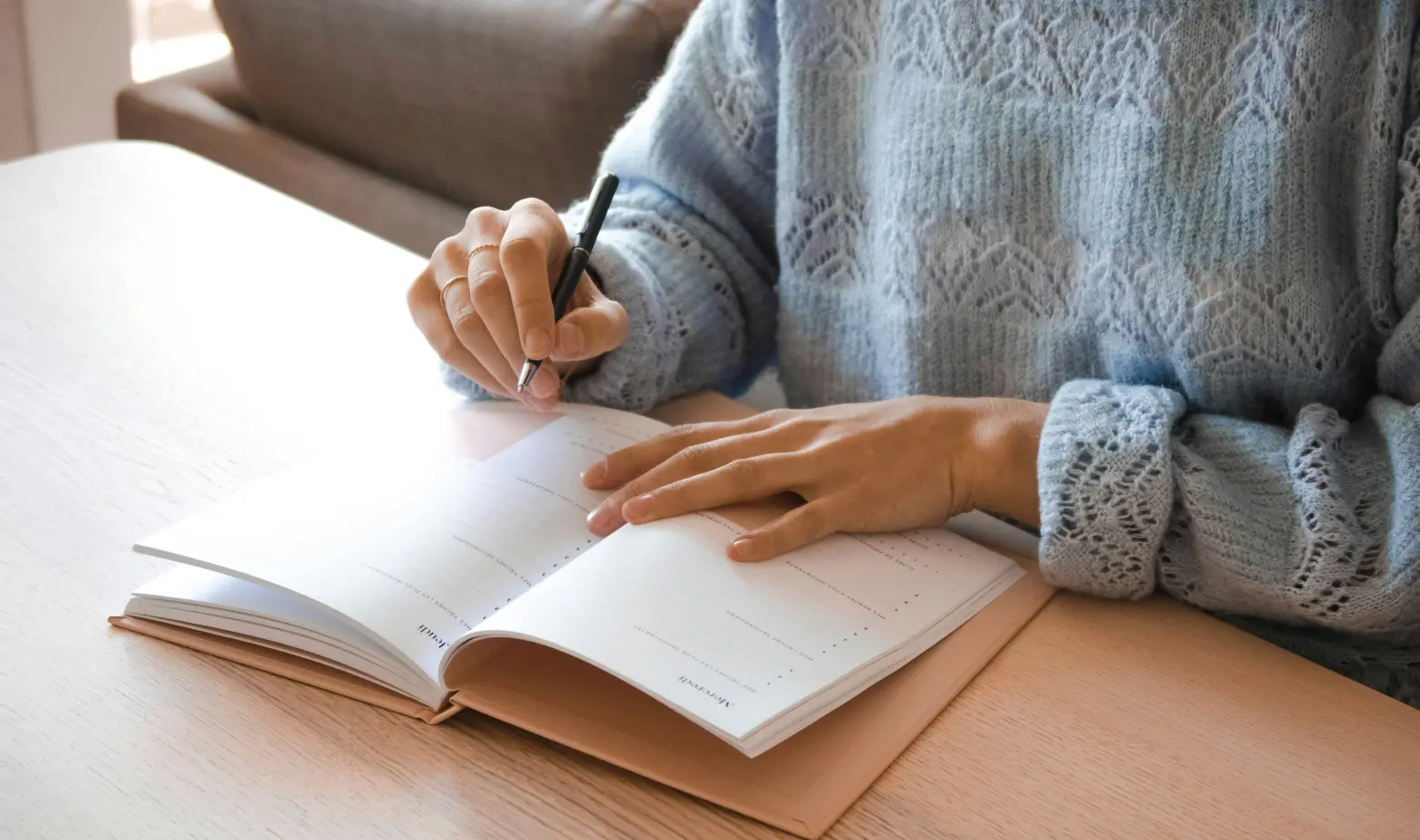 Woman seated at a desk, writing in a notebook with a pen, focused on her task.