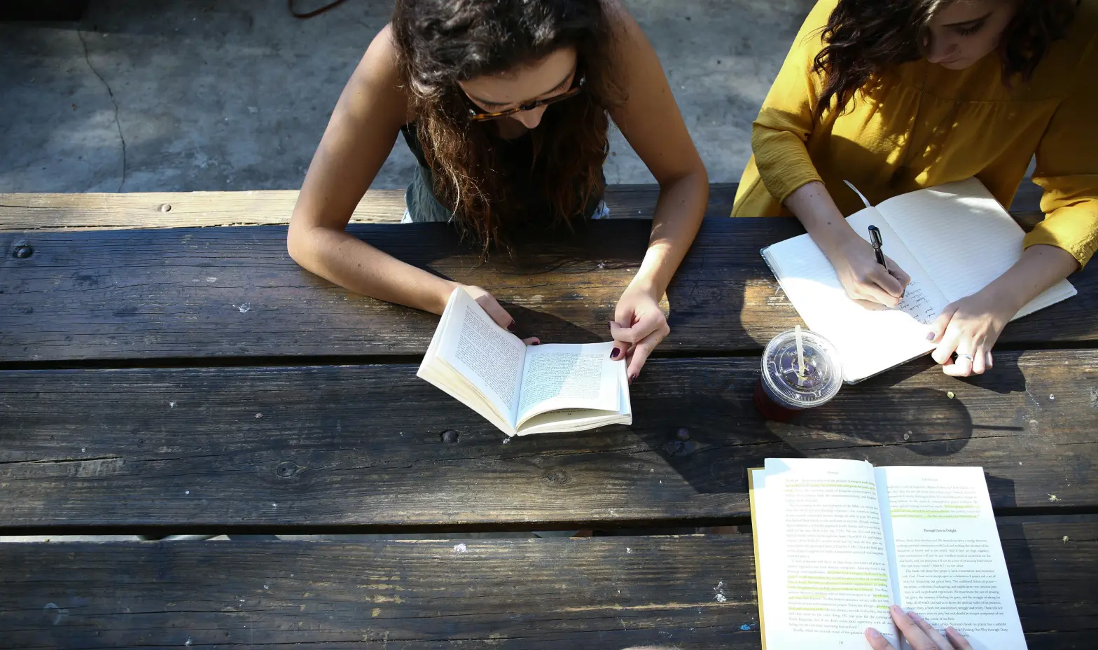 Two individuals seated at a table, engrossed in reading their books.
