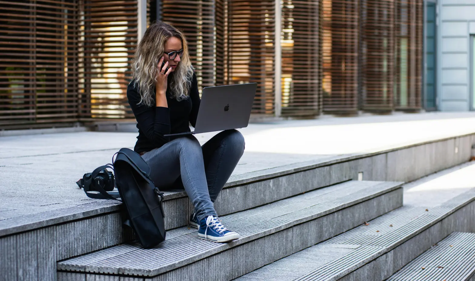 A woman casually seated on steps, working on her laptop, enjoying the moment.