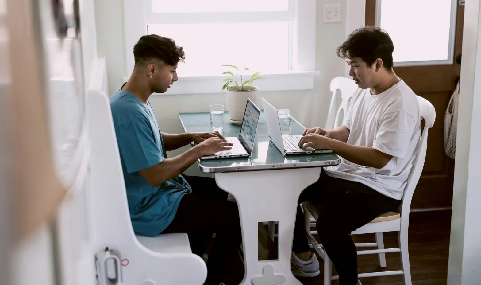Two men seated at a table, each using a laptop, engaged in discussion.