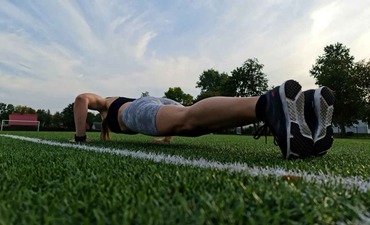 A woman doing push-ups on green grass, focusing on her workout in a sunny outdoor setting.