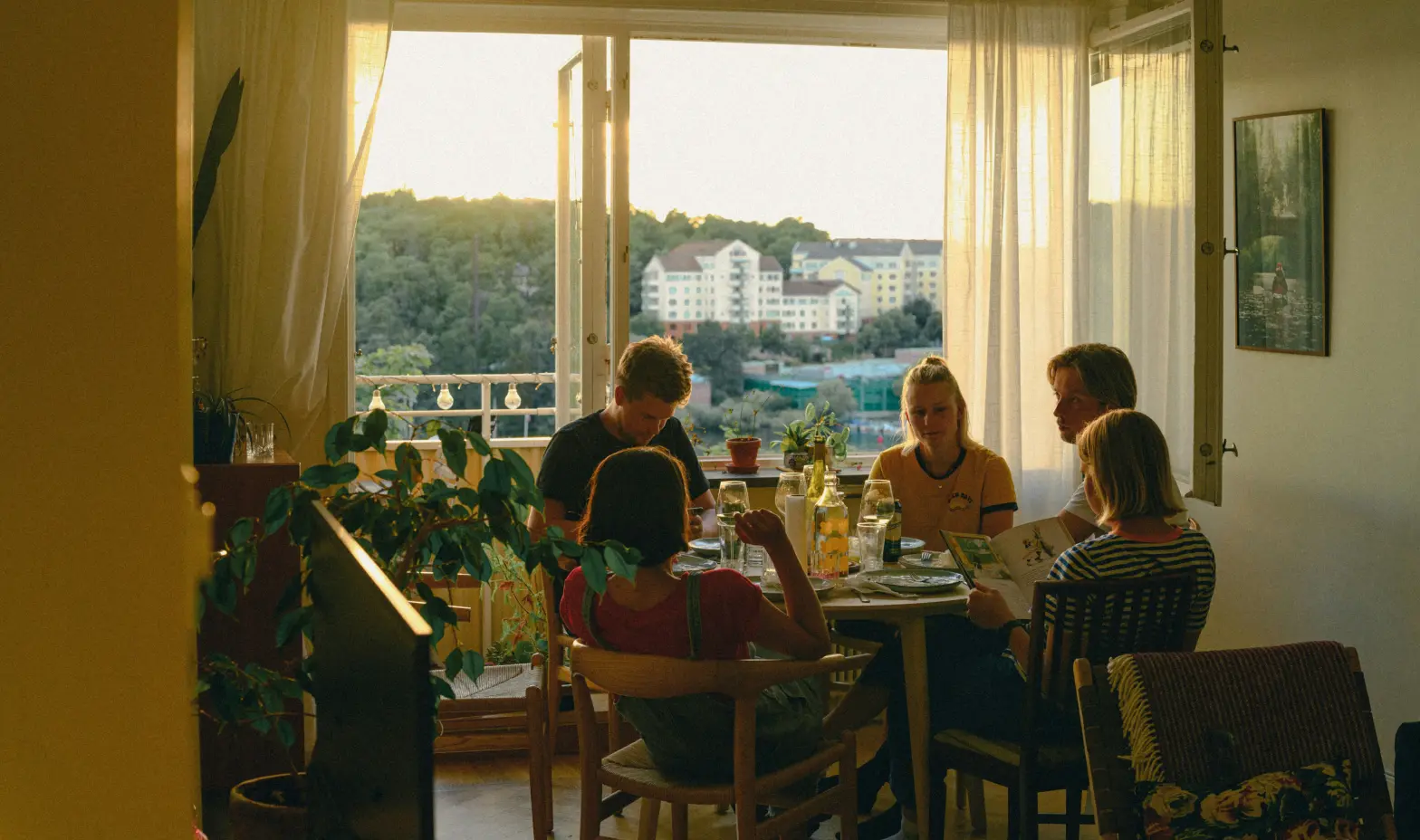 Friends enjoy a meal together at a sunlit table overlooking a city.