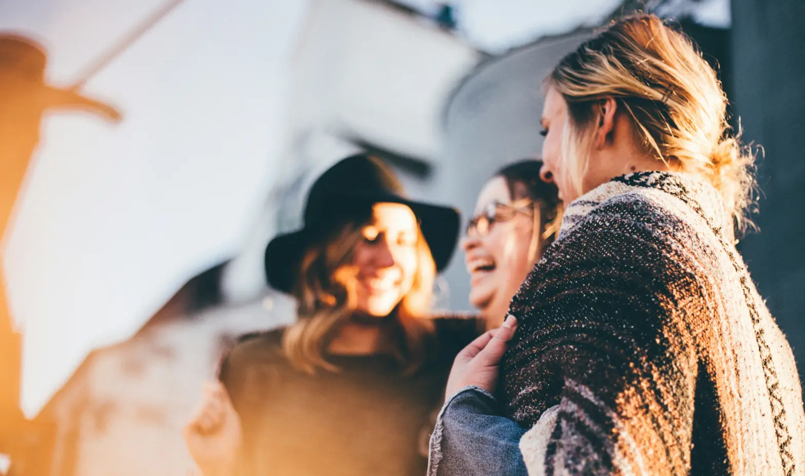 Three women stand together smiling in front of a modern building.