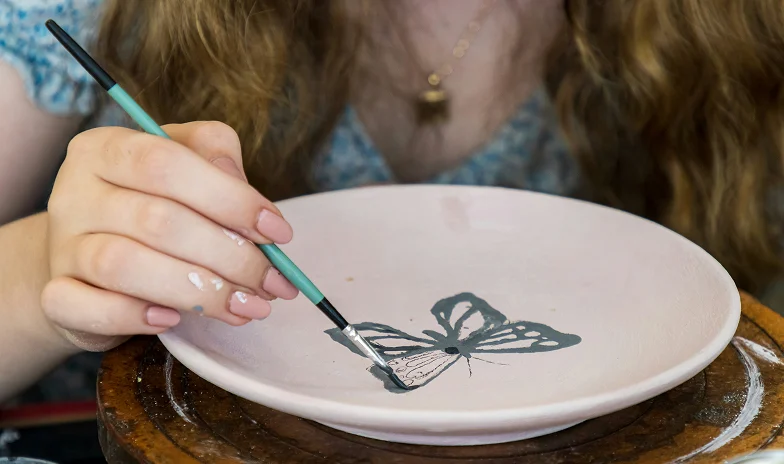 painting a butterfly on handmade pottery