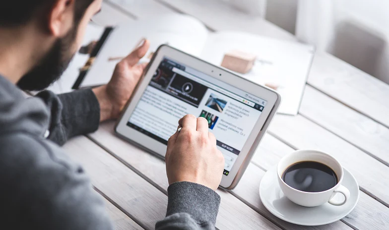 Person reading news on a tablet while drinking coffee