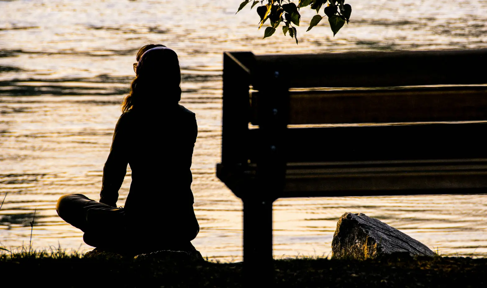 A woman relaxes near the bench, enjoying the serene view of the water beside her.